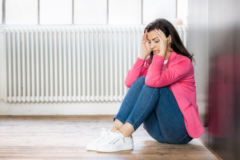 Frau sitzt am Boden mit Händen am Kopf